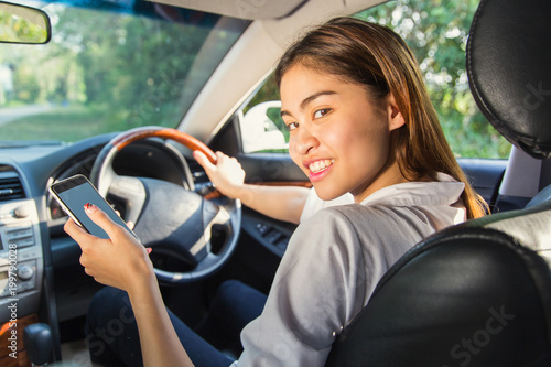 Beautiful asian woman smiling and using navigation app on smartphone while driving a car