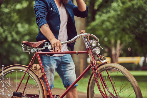 Male dressed in casual clothes, walking with a retro bicycle in a city park.