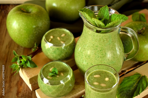 Green smoothie in glass vessels on wooden background
