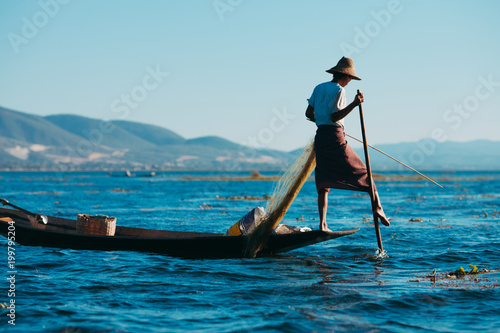 Fisherman on Inle Lake, Burma. Rowing with his foot. Background cascade of mountains and red dawn.