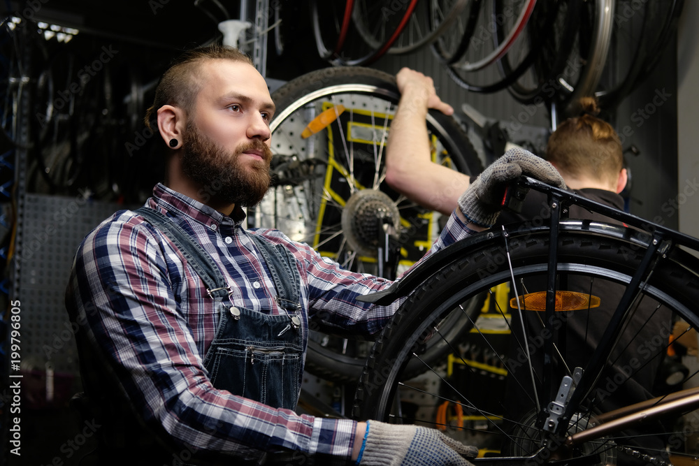 Two handsome stylish male working with a bicycle in a repair shop. Workers repair and mounts bike in a workshop Two handsome stylish male working with a bicycle in a repair shop. Workers repair and mounts bike in a workshop