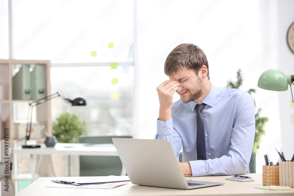 Young man suffering from headache in office Young man suffering from headache in office