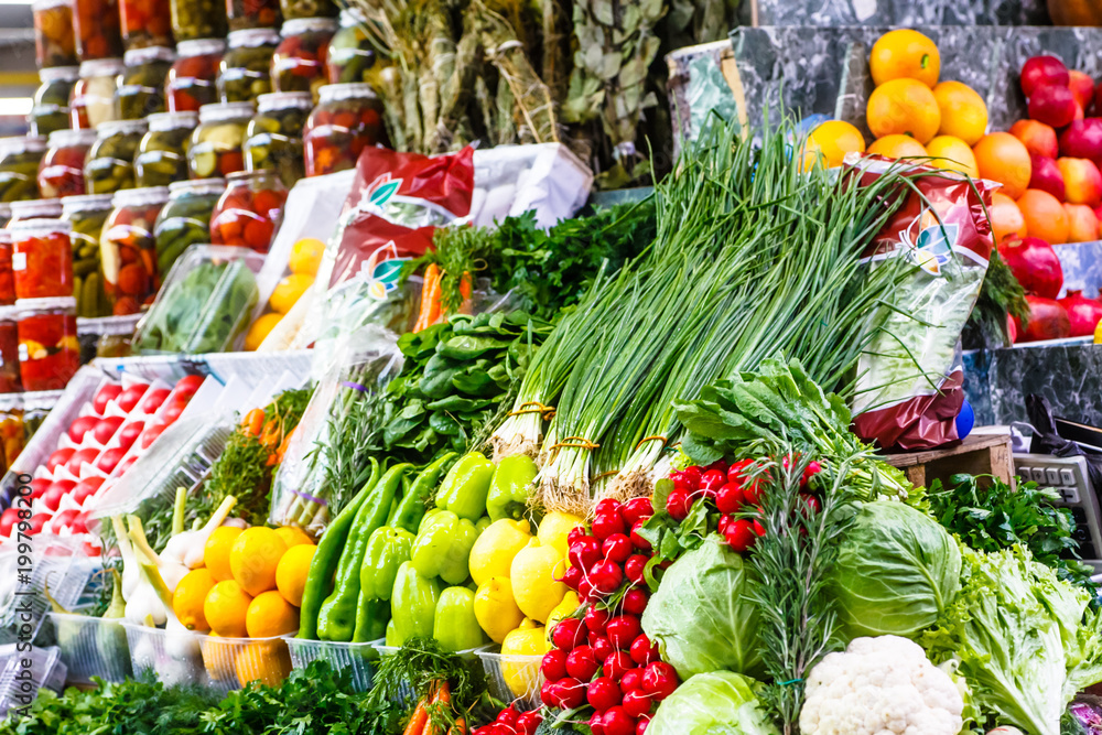 A lot of different vegetables and fruits are on the shelves in the market.
