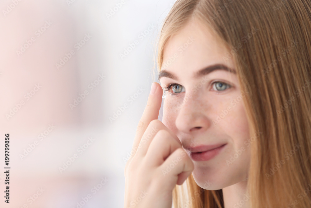Teenage girl putting contact lens in her eye on blurred background Teenage girl putting contact lens in her eye on blurred background