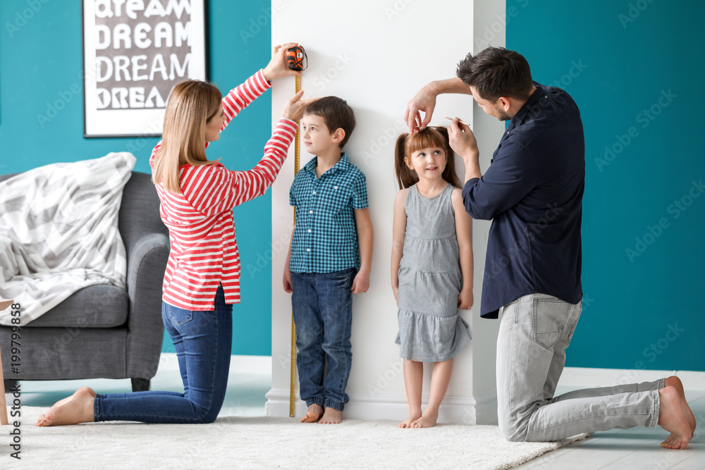 Parents measuring height of their children at home - obrazy, fototapety, plakaty 