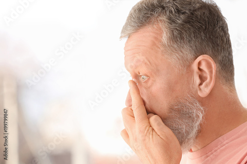 Senior man putting contact lens in his eye on blurred background