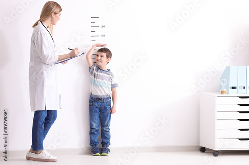 Female doctor measuring height of little boy in clinic photo