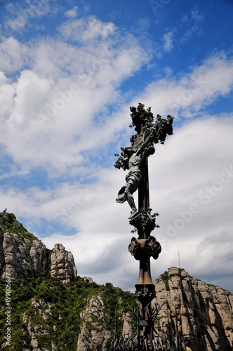 Cross with crucifixion of Jesus Christ on a mountain trail near Montserrat Monastery. The Montserrat mountain with strange weathered rocks. Catalonia, Spain.