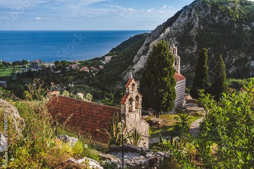 Stone church with bell tower at Gradiste monastery near Buljarica, Montenegro. Churchyard and abbey near Adriatic sea and mountains under evening lights. photo