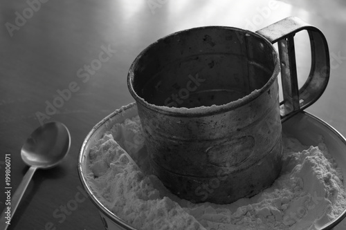 Fotografie Old stainless steel cup flour sifter lies in a white enamel bowl on an old scrat