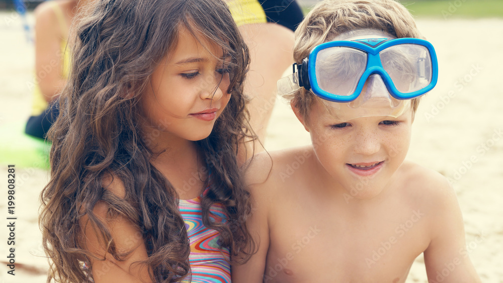 Portrait of children on the beach in summer. Little girl sitting with er frend on the sand and smiling. Portrait of children on the beach in summer. Little girl sitting with er frend on the sand and smiling.