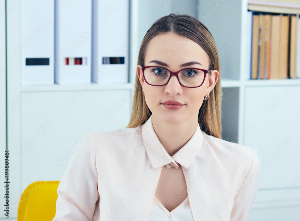 Portrait of young serious businesswoman looking at the camera while using laptop in office. Portrait of young serious businesswoman looking at the camera while using laptop in office.