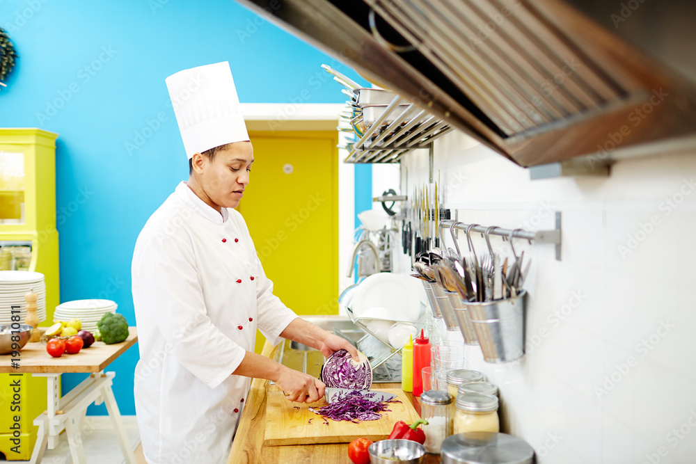 Young chef chopping fresh purple cabbage while standing by table for preparing food in the kitchen Young chef chopping fresh purple cabbage while standing by table for preparing food in the kitchen