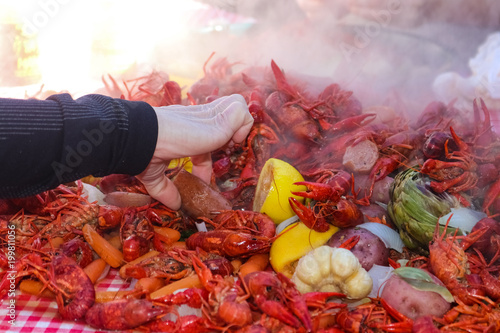 Photography A hand reaching into a pile of steaming food piled on a table at a crawfish boil