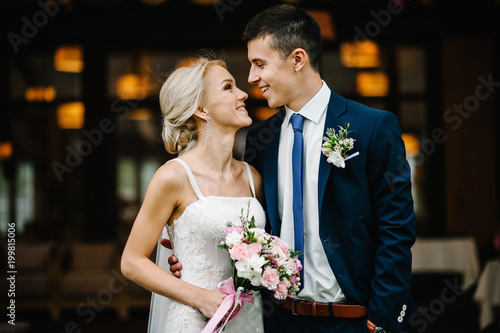 Romantic couple newlyweds, bride and groom holding bouquet of pink and purple flowers and greens with ribbon at the wedding ceremony. Happy and joyful wedding moment.