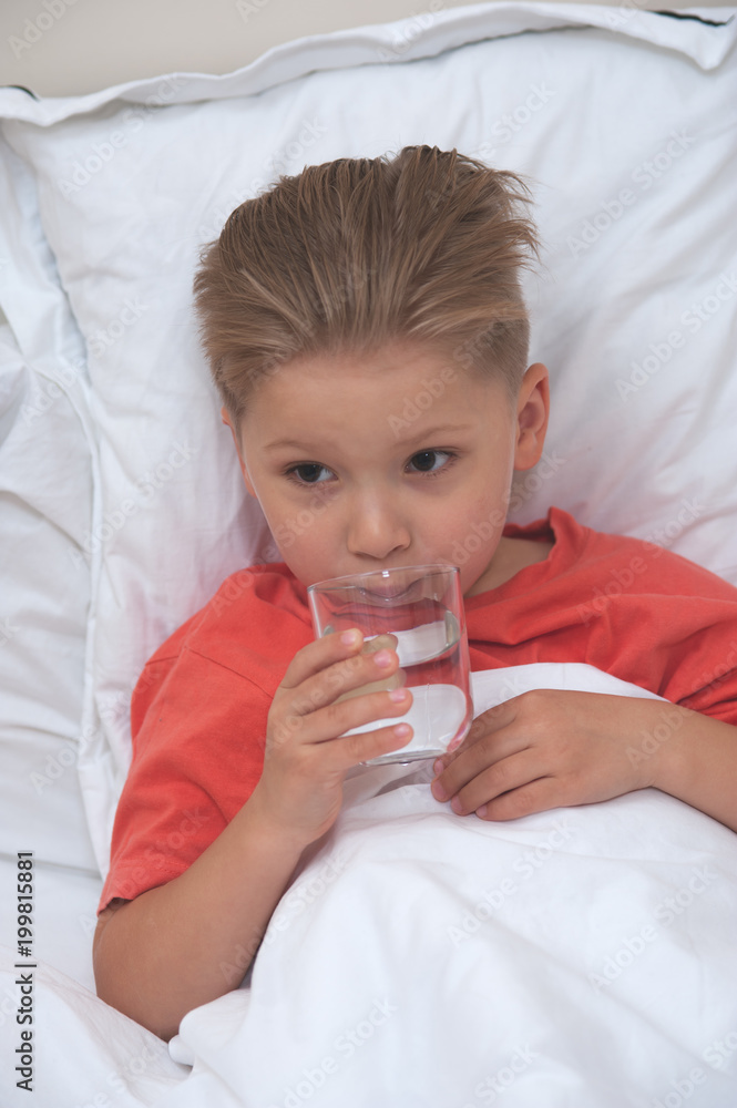 Little sick cute cboy holding a pill and a glass of water lying on the bed Little sick cute cboy holding a pill and a glass of water lying on the bed