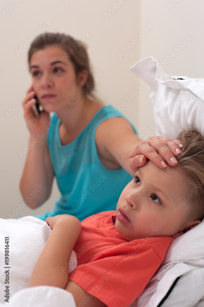 Worried young woman in a blue dress is calling to the doctor on phone on the background of sick little boy lying in bed. Worried young woman in a blue dress is calling to the doctor on phone on the background of sick little boy lying in bed.