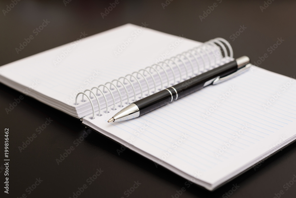 Notepad and pen on black wooden table. These objects are much used in school, in notes and small jobs. Notepad and pen on black wooden table. These objects are much used in school, in notes and small jobs.