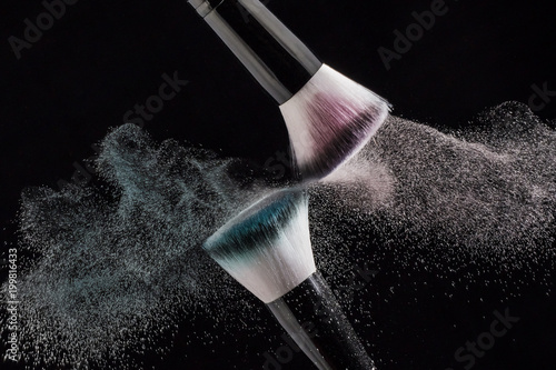 Makeup brushes with red and green powder explode on a black background