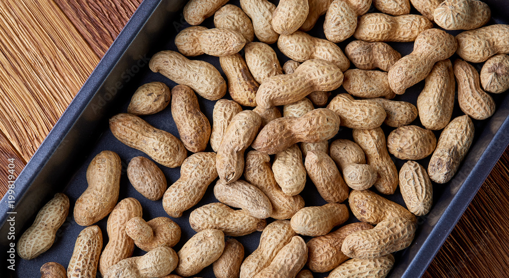 Unpeeled raw peanut on baking tray over wooden background, selective focus, shallow depth of field. Unpeeled raw peanut on baking tray over wooden background, selective focus, shallow depth of field.