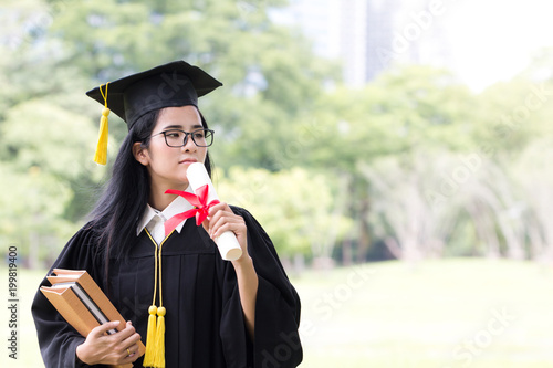 Happy graduate young Asian woman in cap and gown holding certificate in hand, Education concept