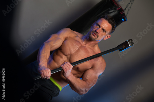 Functional training. Muscular strong man with naked torso training with hammer and tyre.