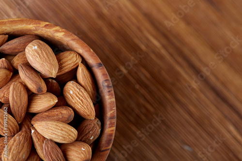 Bowl of almonds on wooden background, top view, close-up, selective focus.