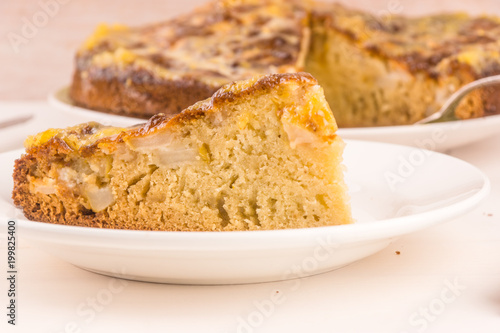 A piece of French apple cake on a plate on a light wooden background