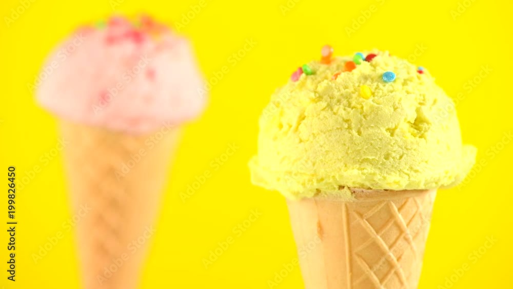 Ice cream. Vanilla, banana or lemon flavor icecream in waffle cone rotated over yellow background. Sweet dessert decorated with colorful sprinkles closeup. 4K UHD video footage. 3840X2160 Ice cream. Vanilla, banana or lemon flavor icecream in waffle cone rotated over yellow background. Sweet dessert decorated with colorful sprinkles closeup. 4K UHD video footage. 3840X2160
