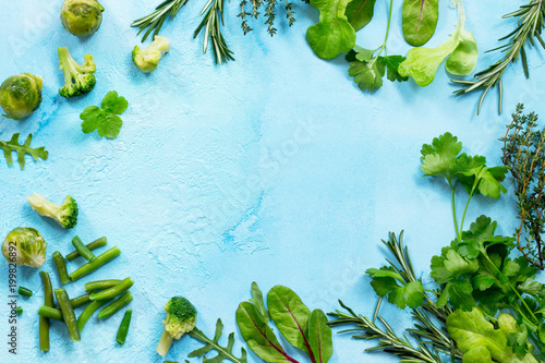 Food background. Various summer green vegetables, spices and fresh herbs on blue concrete background. Copy space, top view flat lay background.