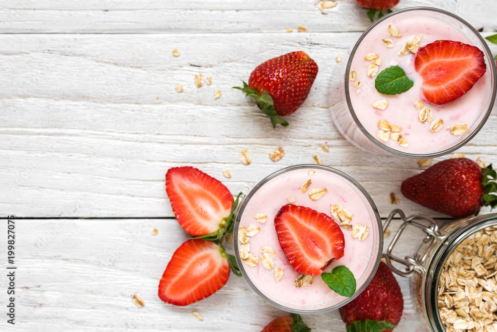 two glasses of healthy strawberry yogurt with fresh berries, oats and mint on white wooden table two glasses of healthy strawberry yogurt with fresh berries, oats and mint on white wooden table