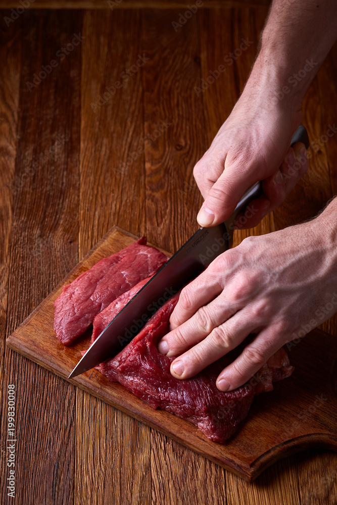 Strong professional man's hands cutting raw beefsteak, selective focus, close-up