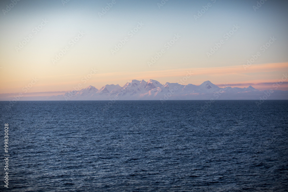 The mountains of Antarctica glow on the horizon as a ship sails away toward the Drake Passage, headed back to Ushuaia, Argentina. The mountains of Antarctica glow on the horizon as a ship sails away toward the Drake Passage, headed back to Ushuaia, Argentina.