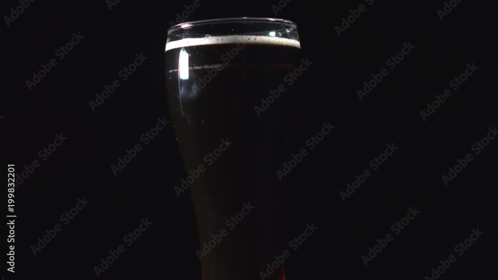 A pint of dark beer is rotating against black background. Glass of stout is spinning A pint of dark beer is rotating against black background. Glass of stout is spinning