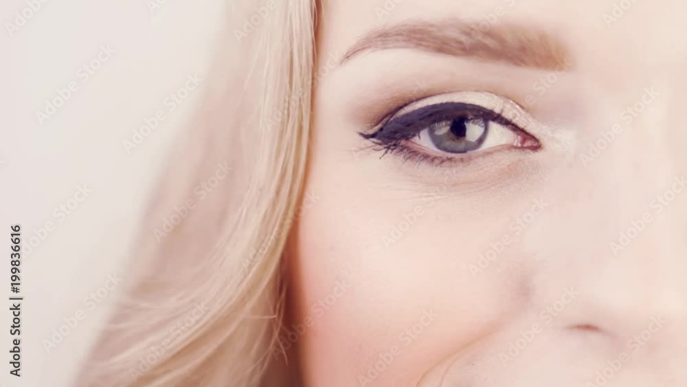 Closeup of girl's eye with beautiful makeup. Girl opens and closes her eye. Professional lighting on face girl in studio. In frame half face, beautiful hairstyle. Closeup of girl's eye with beautiful makeup. Girl opens and closes her eye. Professional lighting on face girl in studio. In frame half face, beautiful hairstyle.