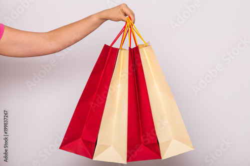 people, sale and consumerism concept - close up of female hand with shopping bags over white background