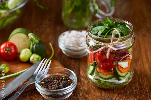 Delicious vegetable salad in jar and fresh veggies on cutting board on table, selective focus, close-up