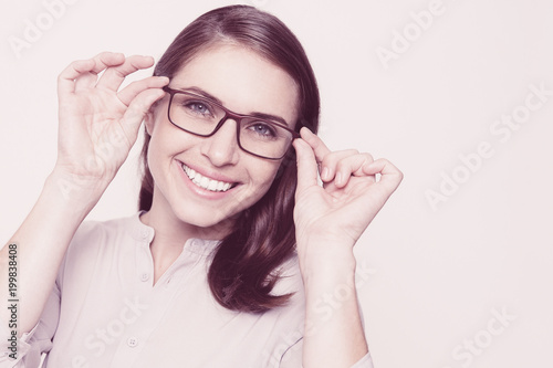Studio portrait of happy young Caucasian woman wearing white shirt trying on eyeglasses, looking at camera and smiling