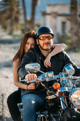 young couple riding a motorcycle and looking at the camera in a desert place. lifestyle concept