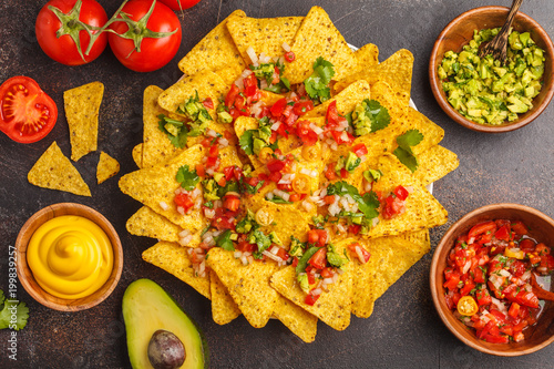 Mexican food concept. Nachos - yellow corn totopos chips with various sauces in wooden bowls: guacamole, cheese sauce, pico del gallo, top view