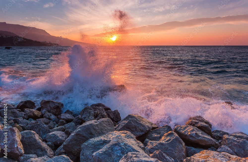 Big sea wave breaks against a stone at sunrise