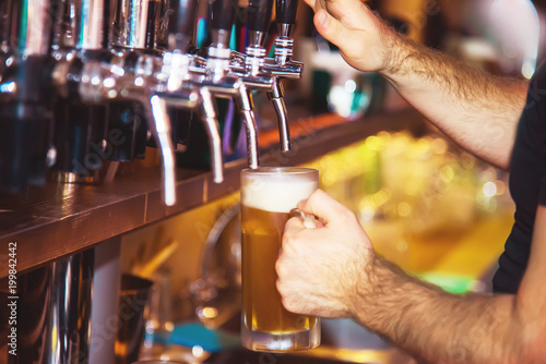 Barman hand at beer tap pouring a draught lager beer serving in a restaurant or pub. Vintage soft effect on photo