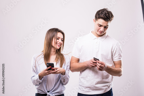 Close up portrait of a interracial smiling couple using mobile phones isolated on the gray background. Woman look at man phones
