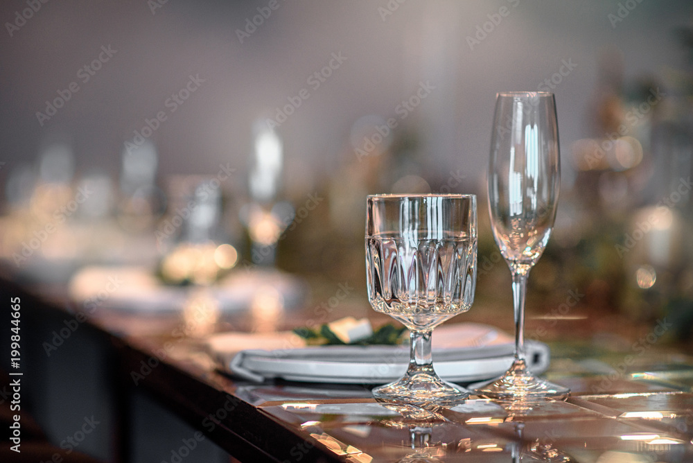 two glasses in the foreground. Mirror table served with plates, forks, spoons, glasses,  napkins in the restaurant. Beautiful festive table decorated with fresh flowers.