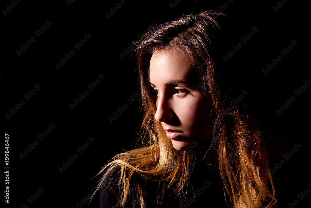 The brown-haired girl with clean skin and long hair looking to side on black background close-up