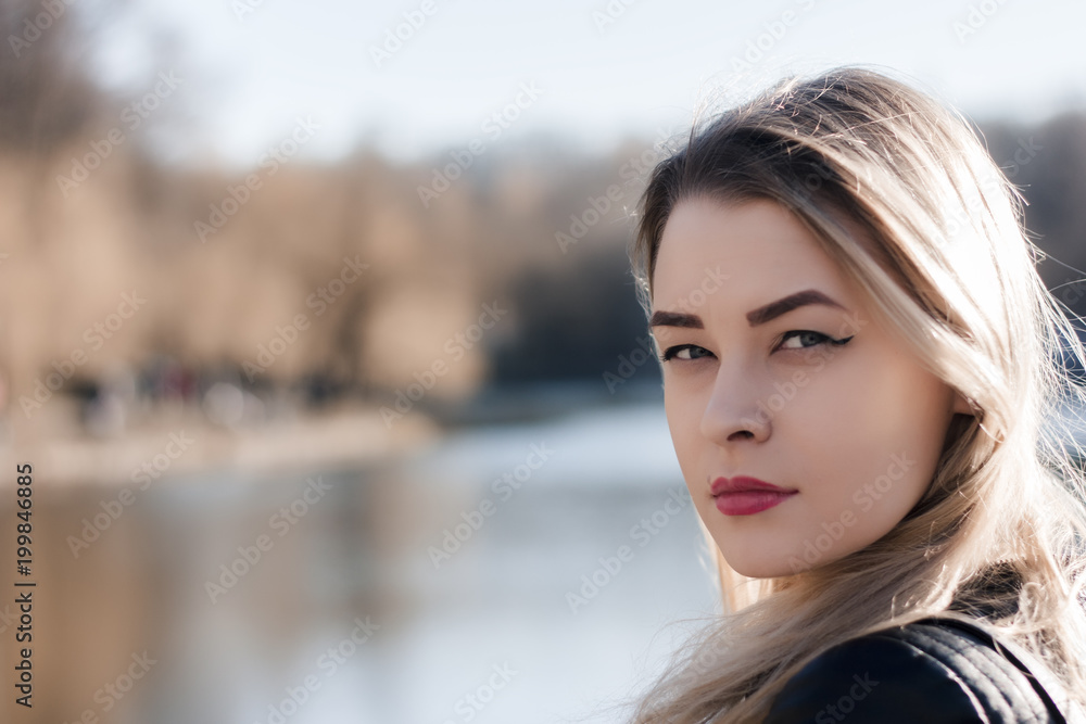 Outdoors portrait of beautiful young brunette girl. Woman smiling happy on sunny summer or spring day outside on city background. Close-up portrait in a golden hour. Selective focus. Outdoors portrait of beautiful young brunette girl. Woman smiling happy on sunny summer or spring day outside on city background. Close-up portrait in a golden hour. Selective focus.
