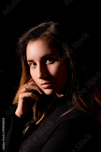 Studio portrait of a brunette girl with hand near chin and professional make-up on black background close-up