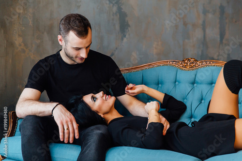 Young beautiful couple in dark clothes on a turquoise vintage couch.