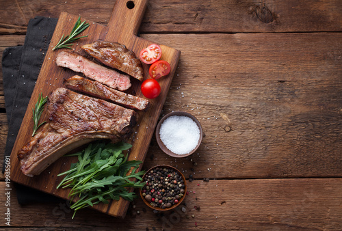Grilled cowboy beef steak, herbs and spices on a rustic wooden background. Top view with copy space for your text photo