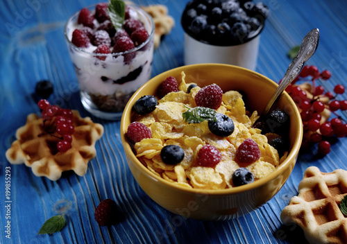 Healthy breakfast with corn flakes, berries, waffle and milk on blue background.